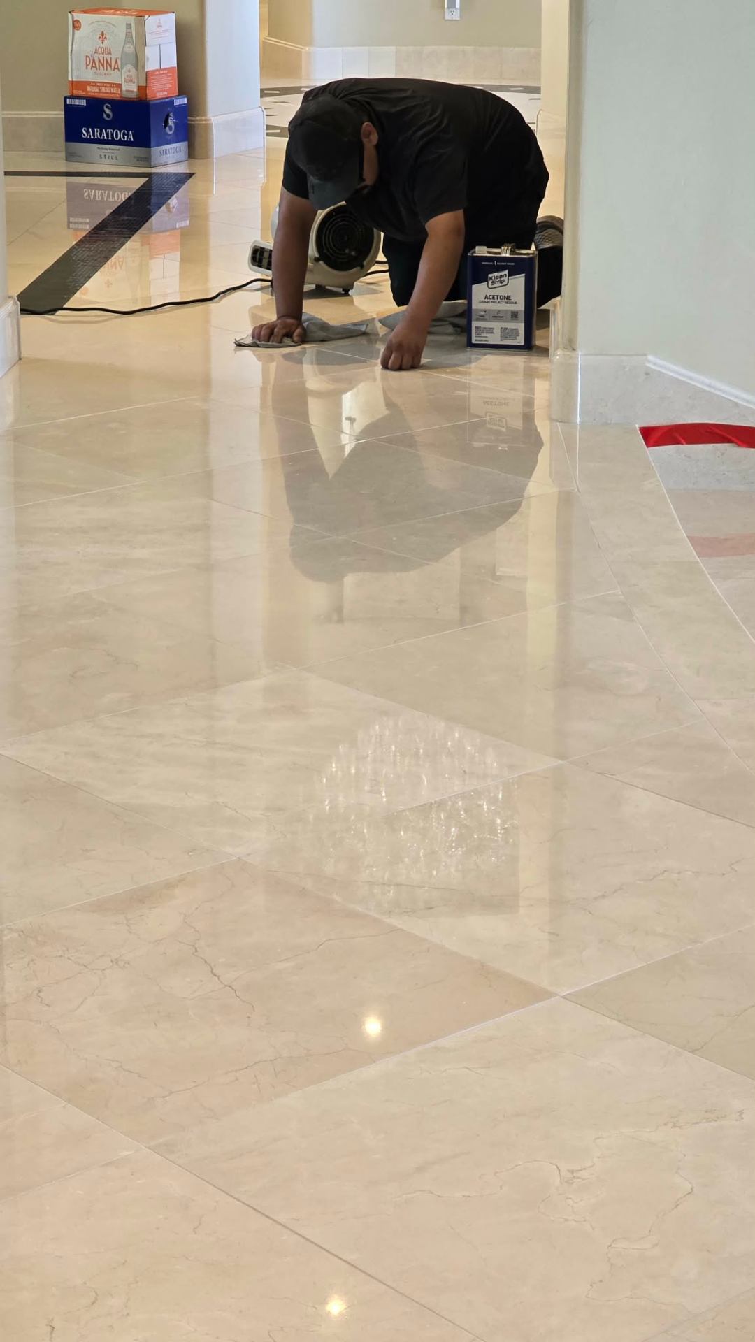Lazona Tile Care technician using acetone and clean cloths to remove adhesive residue from a freshly polished Marmocer veneer marble floor in a Paradise Valley home, with air mover drying the surface and deep reflections visible across the tile