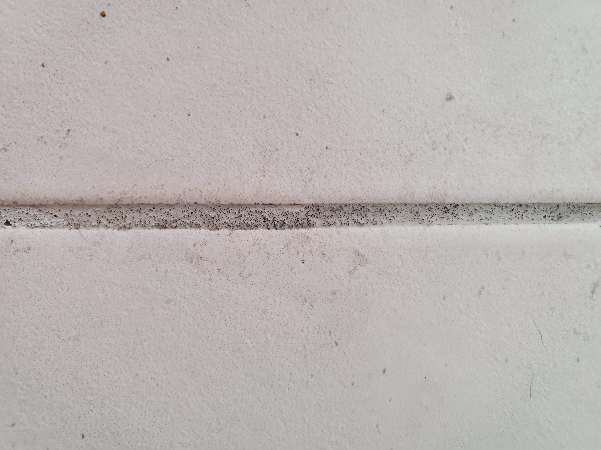 Close-up of powdery cement grout joint between white tile showing pinholes porous surface and dust residue caused by improper mixing and unneutralized grout haze remover in an Arizona new build