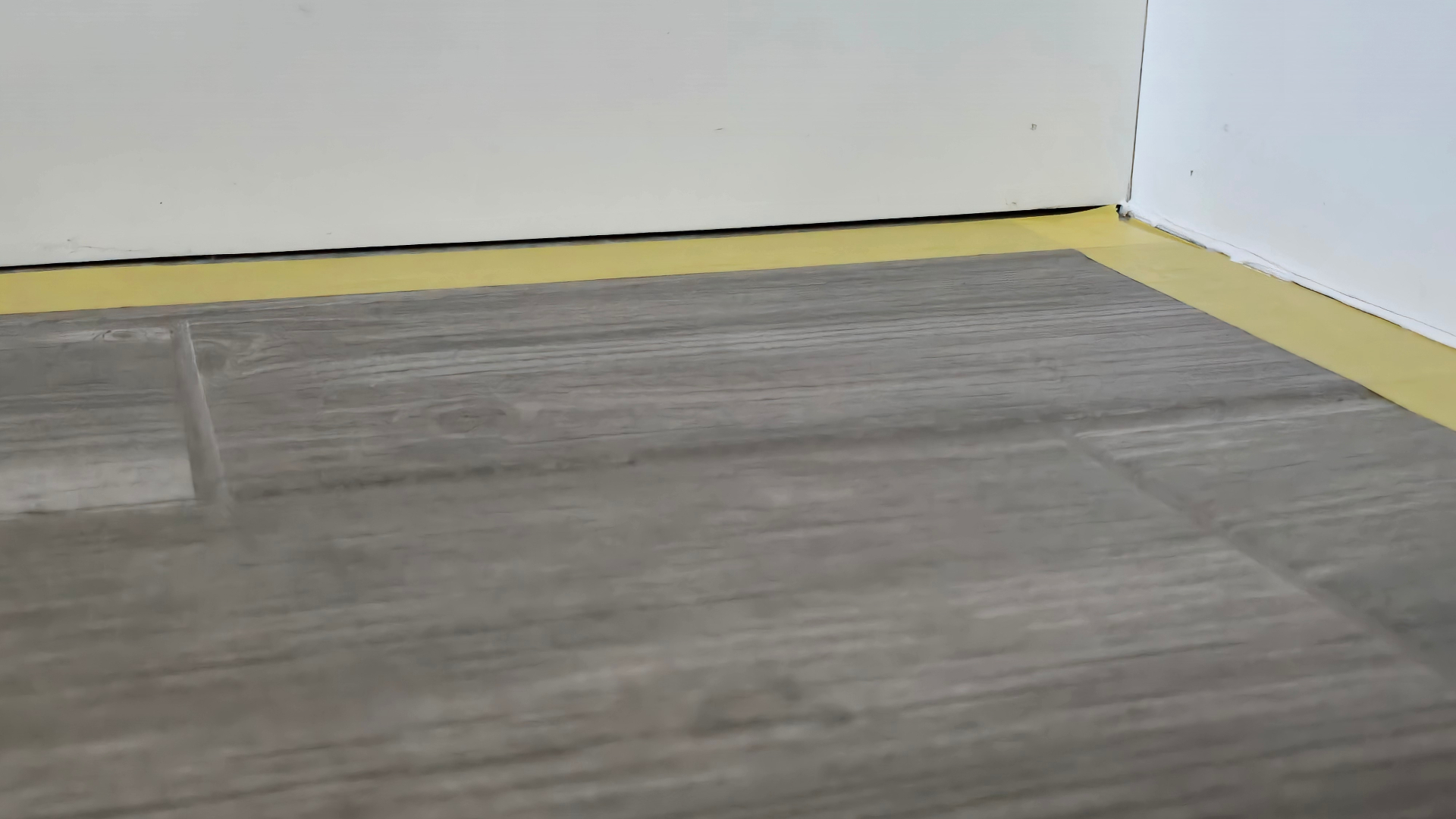 Gray wood-look tile floor at a baseboard showing dull blotchy darkening and uneven shading from grout haze attracting soil in an Arizona new build home