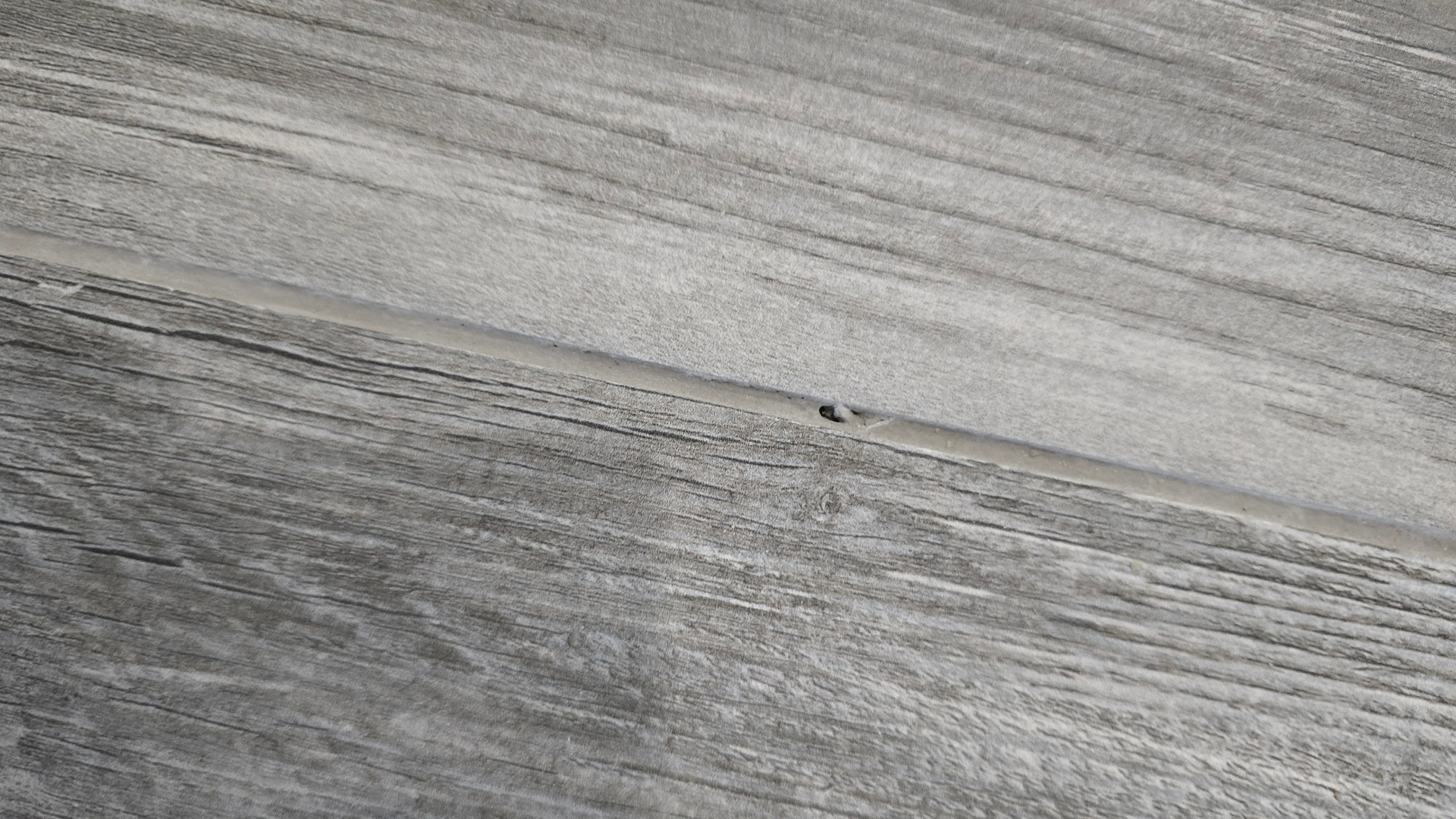Close-up of powdery, chalky grout joint between gray wood-look porcelain planks in an Arizona new build home showing surface erosion and pinholing